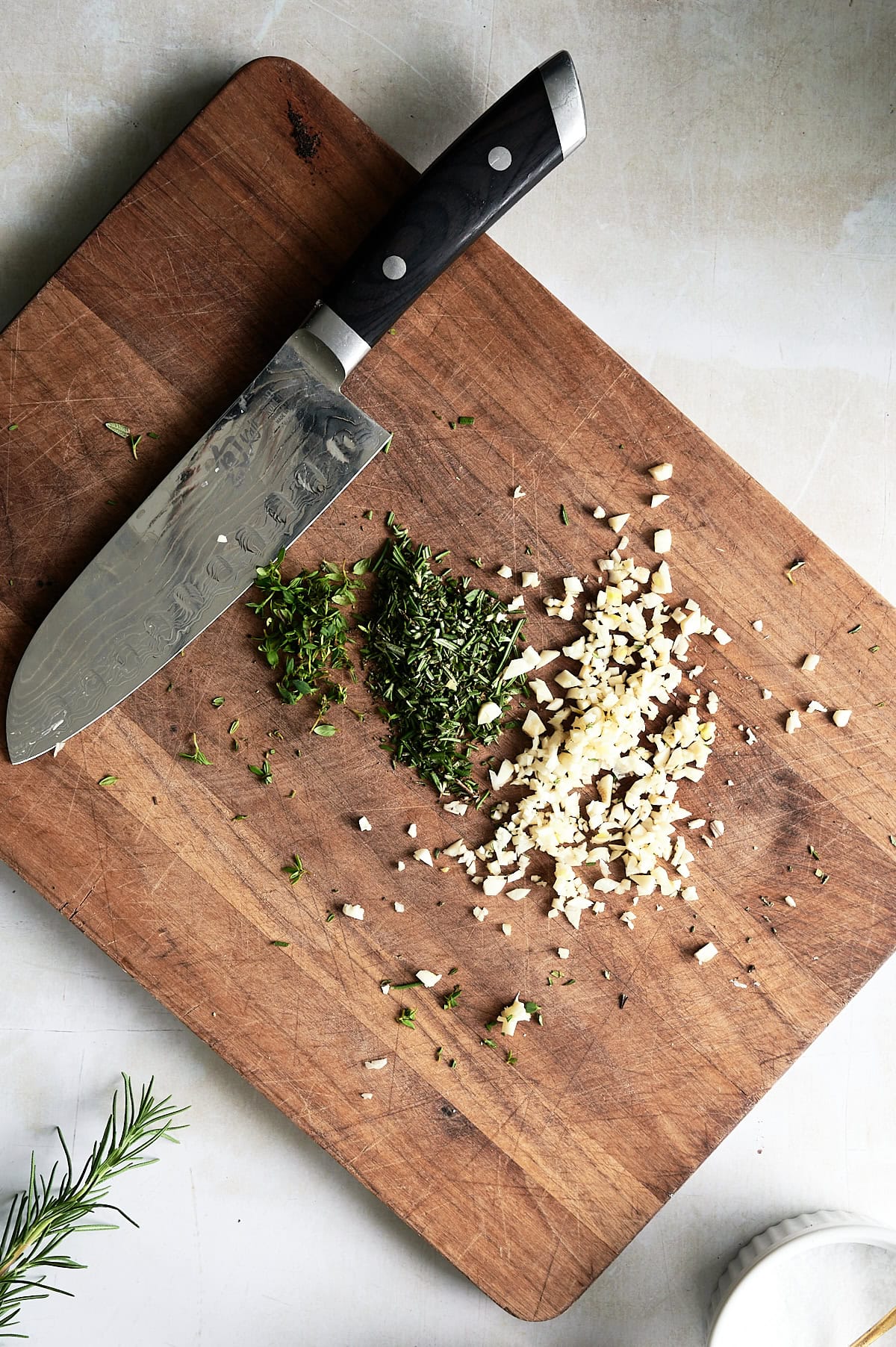 wooden board with a knife and minced garlic and rosemary.