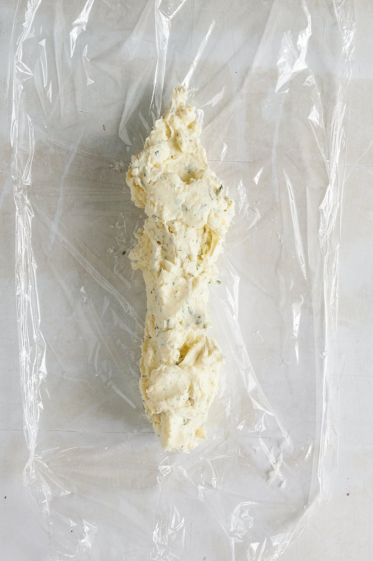 piece of plastic wrap with compound butter being formed in a log shape.