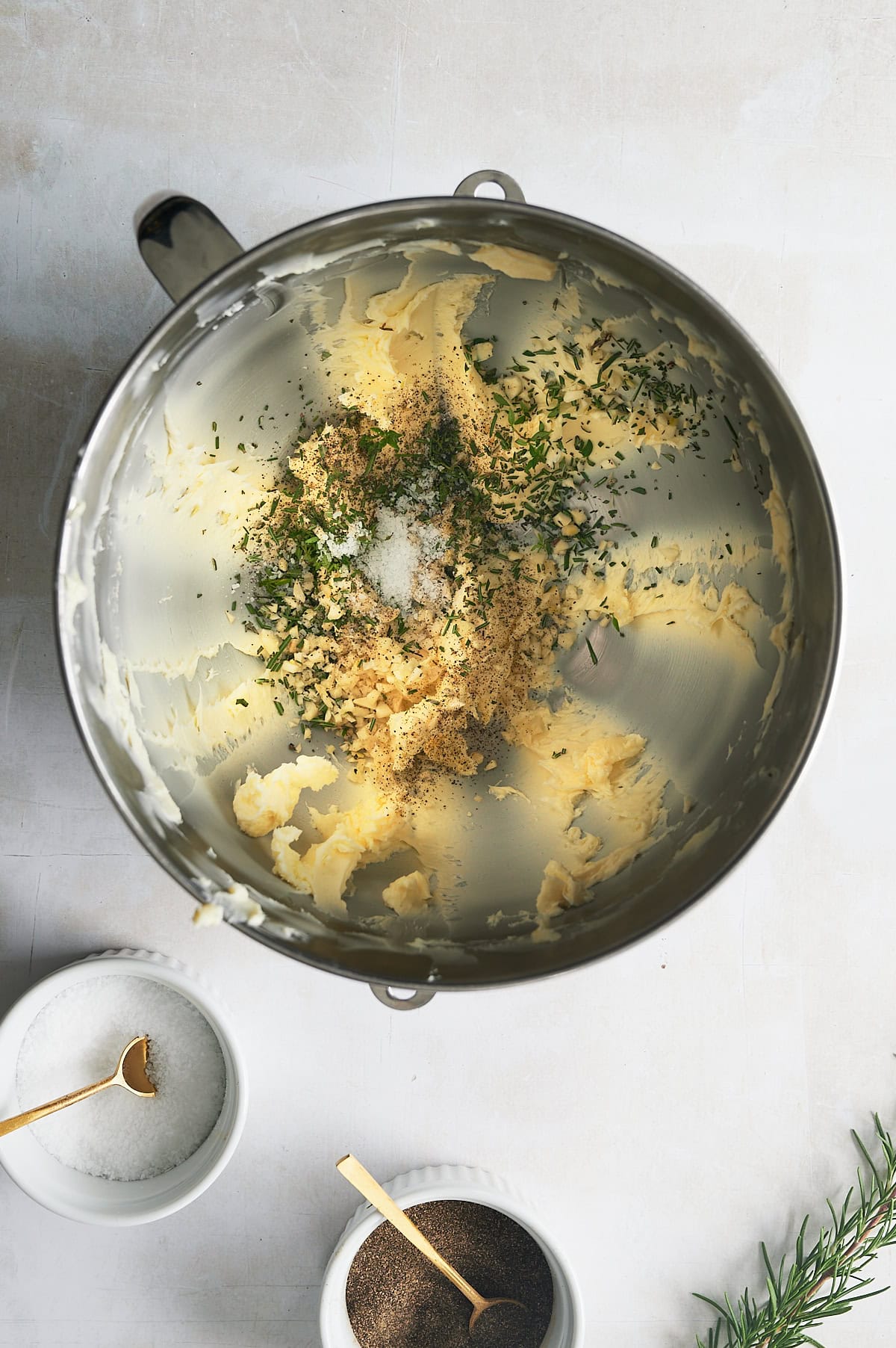 Mixing bowl with whipped butter with herbs, seasoning and bowls of salt and pepper.