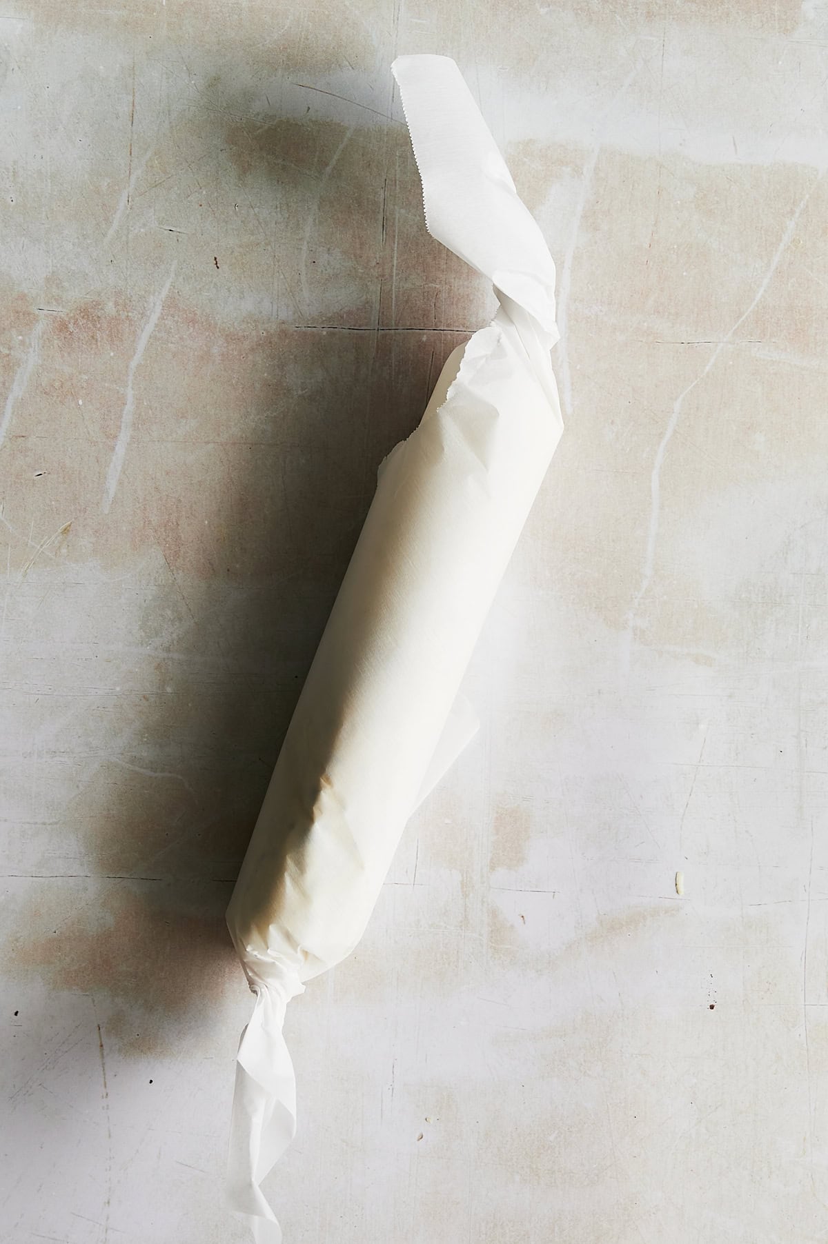 parchment wrapped log of compound butter on a creamy background.