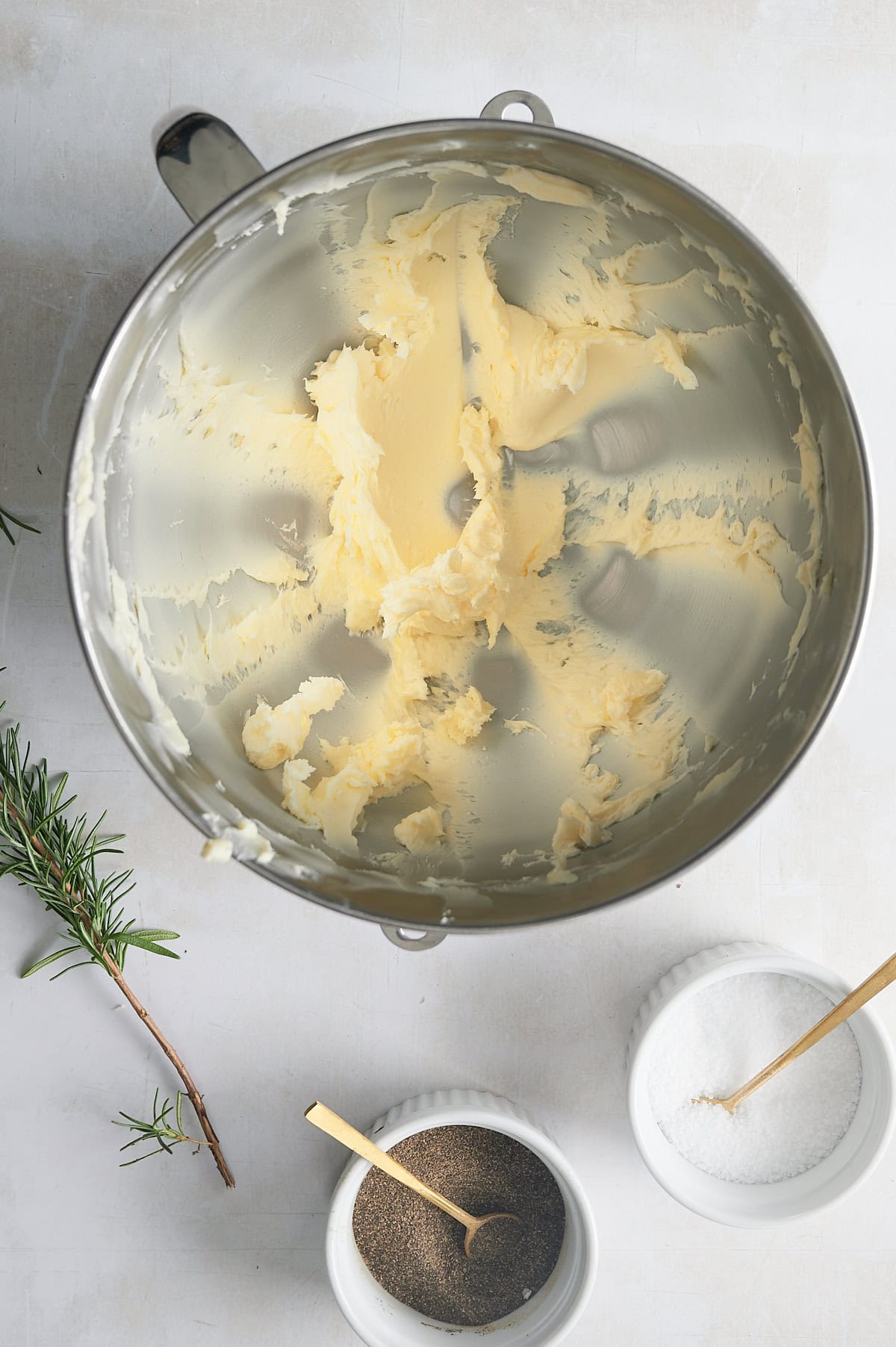 mixing bowl of creamy whipped butter with sprig of rosemary and bowl of salt and pepper.