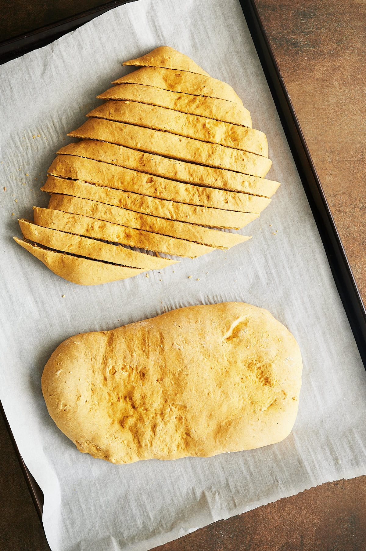 Sliced pumpkin biscotti dough on parchment sheet pan.
