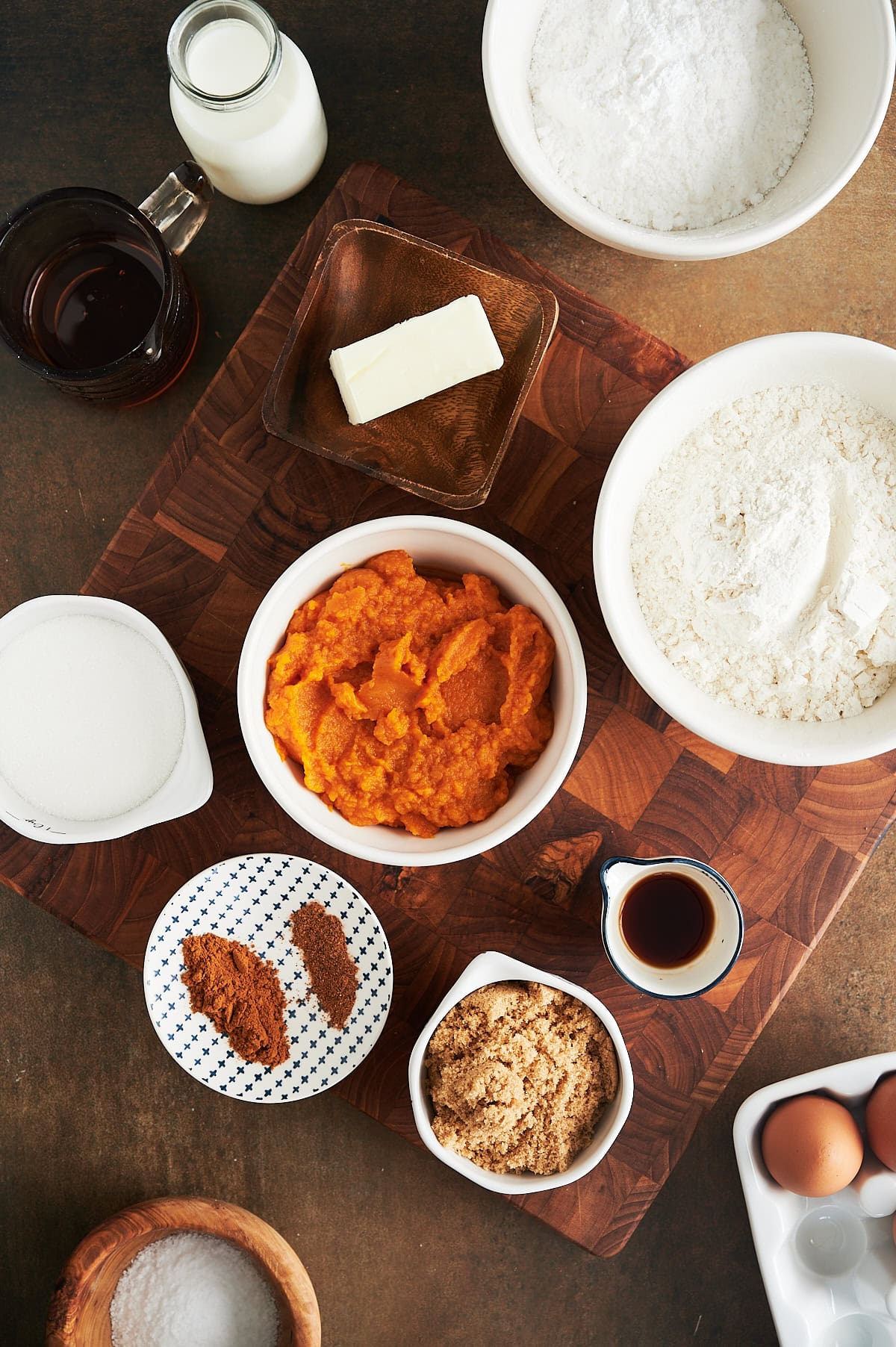 Ingredients for pumpkin biscotti in bowls including pumpkin, spices, sugar, egg on a wooden cutting board.