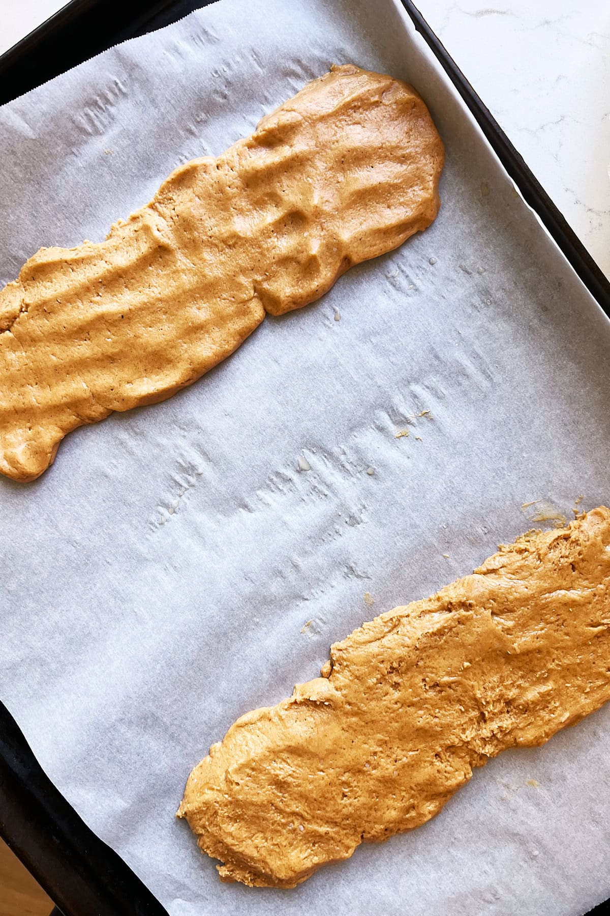 Unbaked pumpkin biscotti dough on parchment sheet pan.