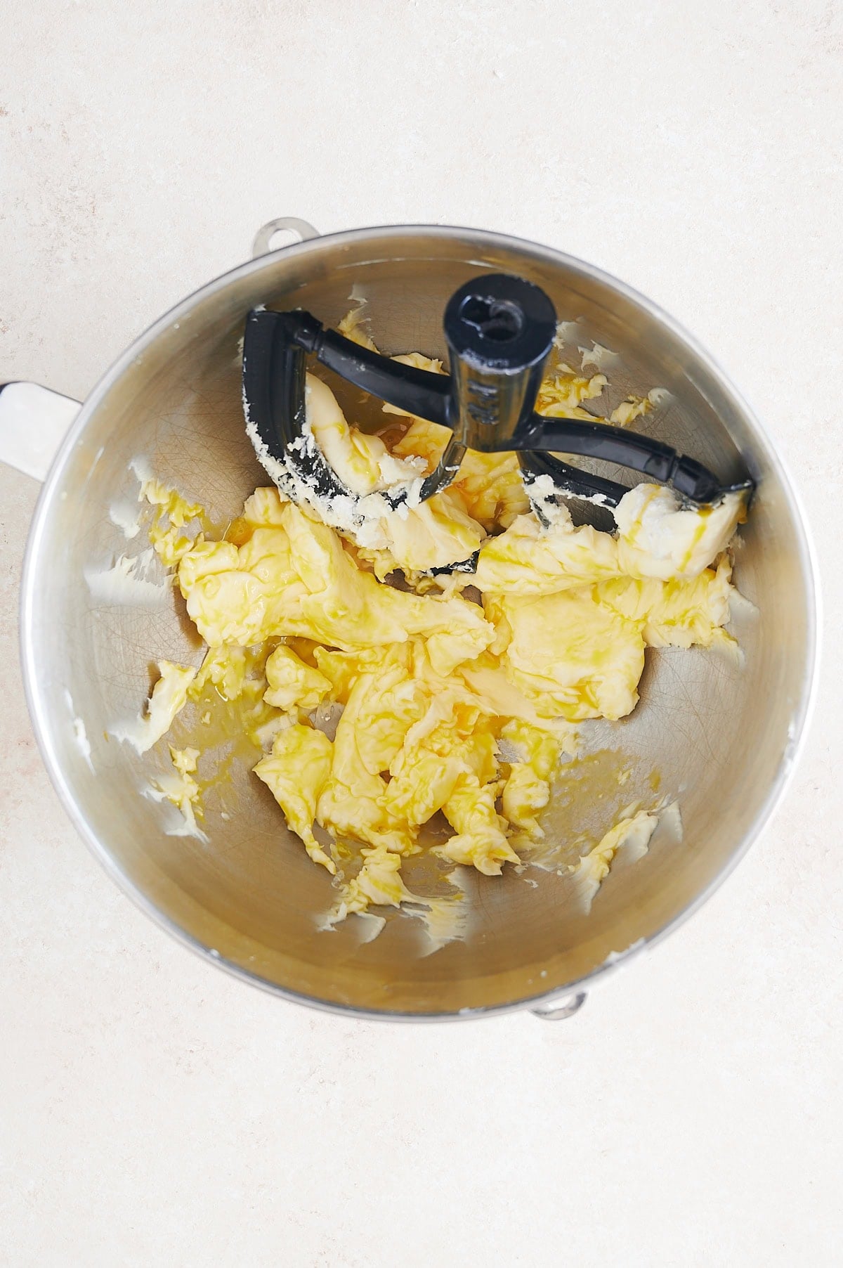 Mixing bowl with butter being creamed with a paddle attachment on a cream background.