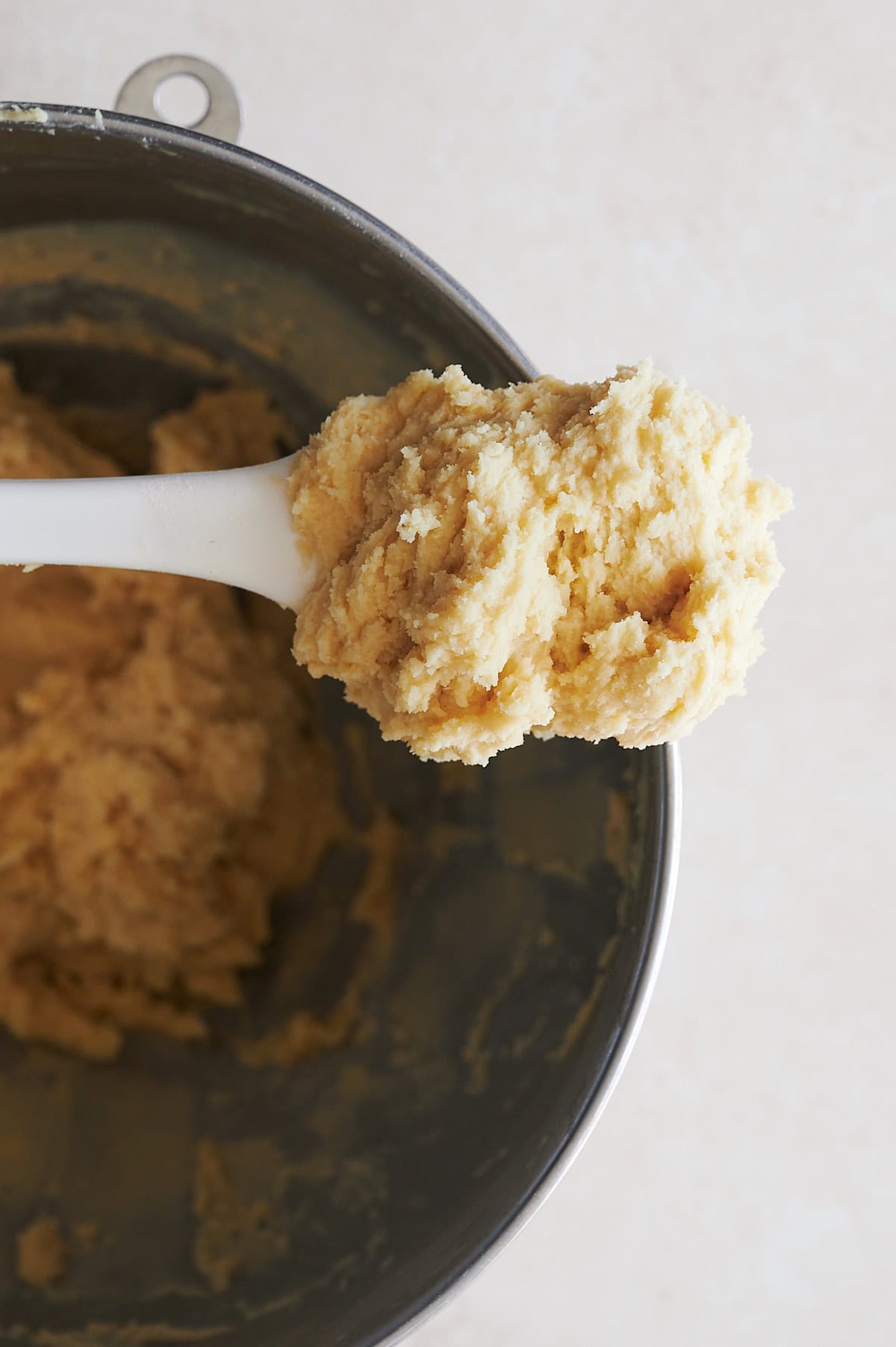 Close up of butter cookie batter on a white spatula over a mixing bowl.