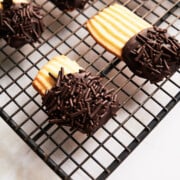 Black wire rack of chocolate sprinkle butter cookies on a cream background.