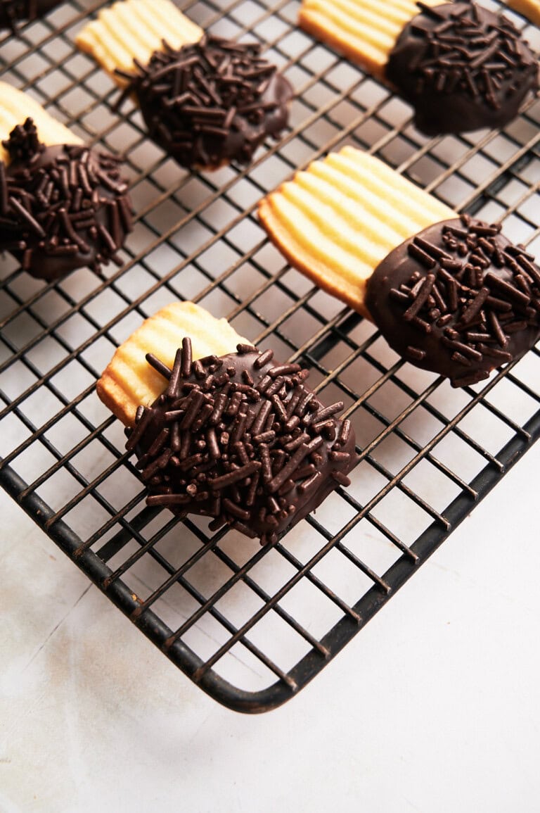 Black wire rack of chocolate sprinkle butter cookies on a cream background.