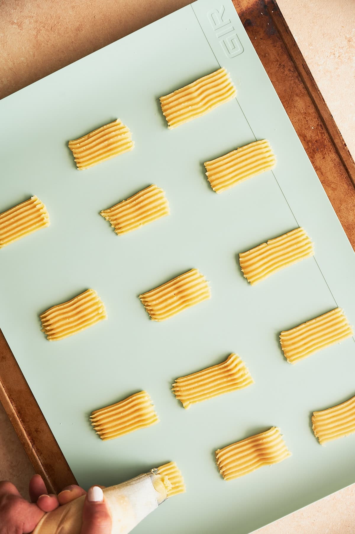 Piping bag piping ribbons of cookie dough on a baking sheet with Tiffany blue silicone mat.