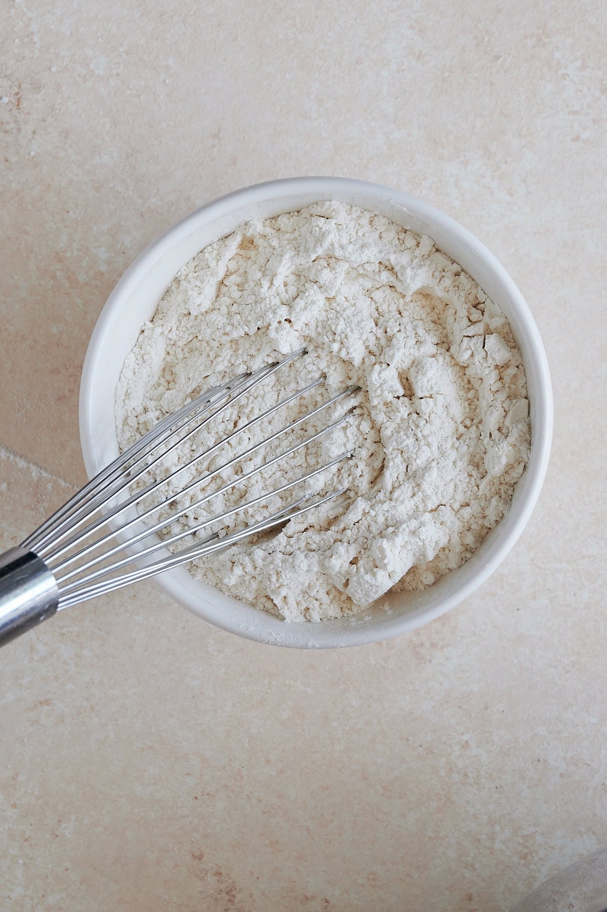 Dry ingredients for cookies being whisked in a white bowl on a cream background.