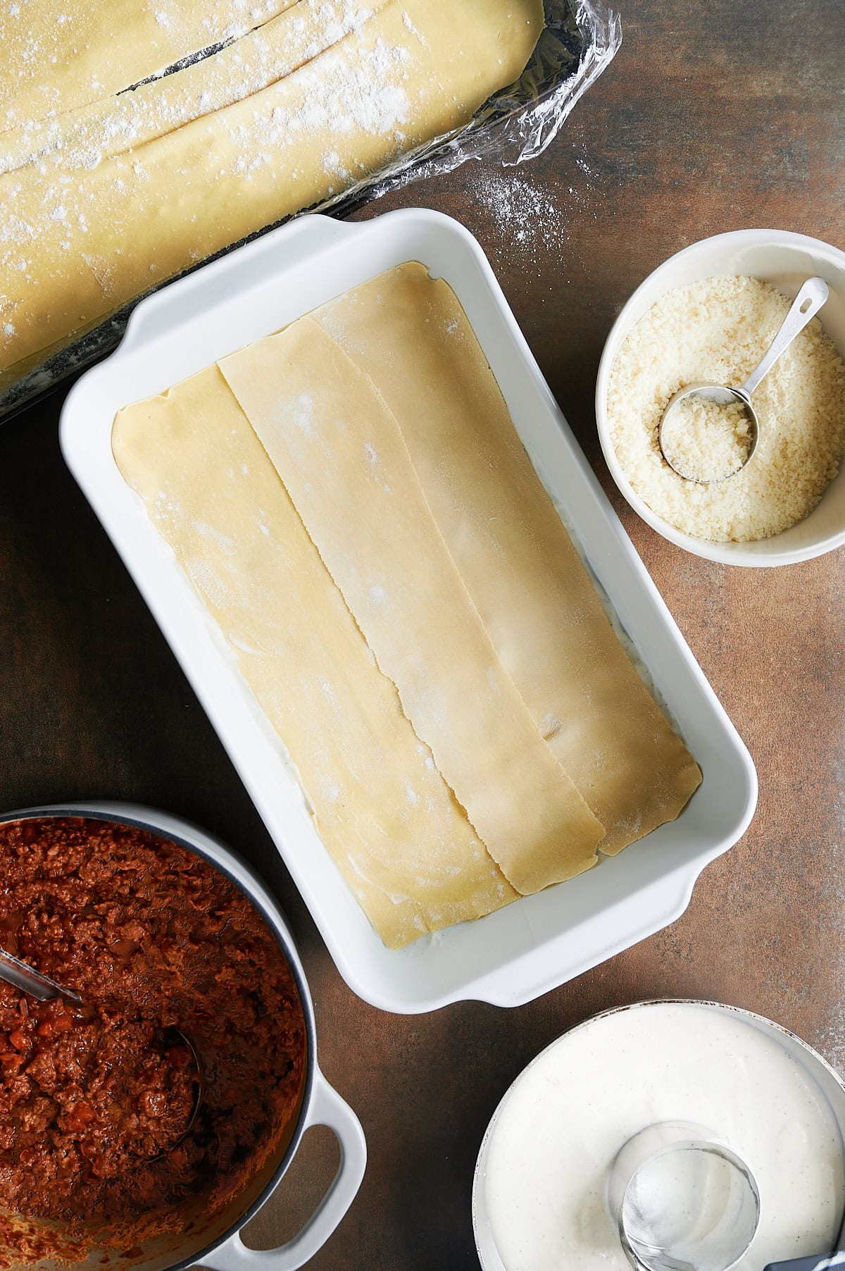 Uncooked lasagna noodles layered in in a baking dish as the base layer for lasagna Bolognese.