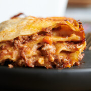 side view of a cut piece of lasagna Bolognese on a black plate.