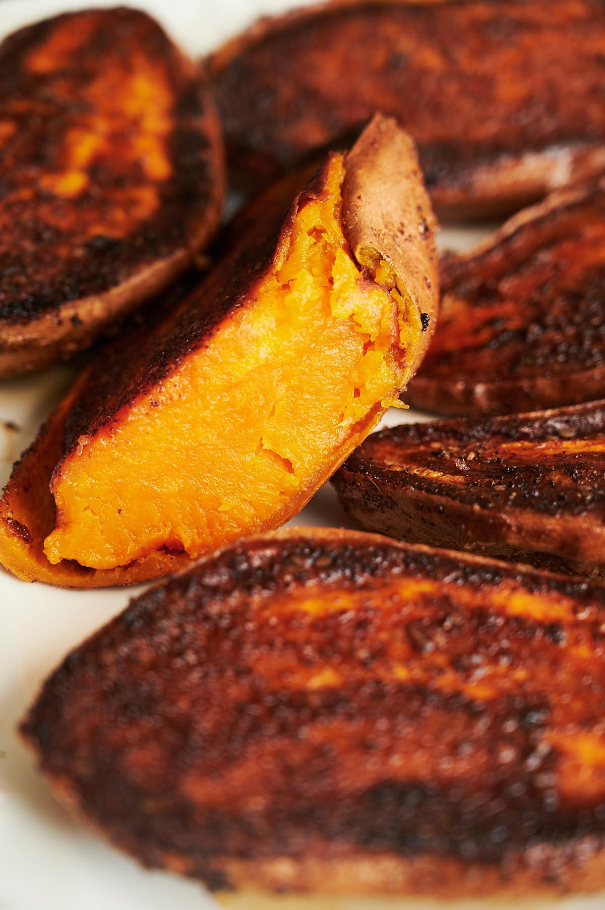 Angled piece of a cut piece of a spicy roasted sweet potato on a white plate.