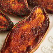 Seasoned and roasted sweet potato halves arranged on a white embossed ceramic plate.