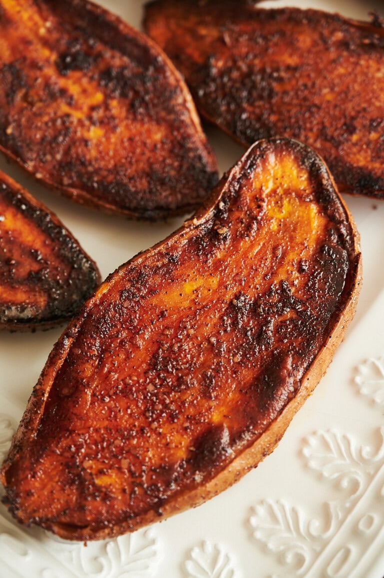 Seasoned and roasted sweet potato halves arranged on a white embossed ceramic plate.