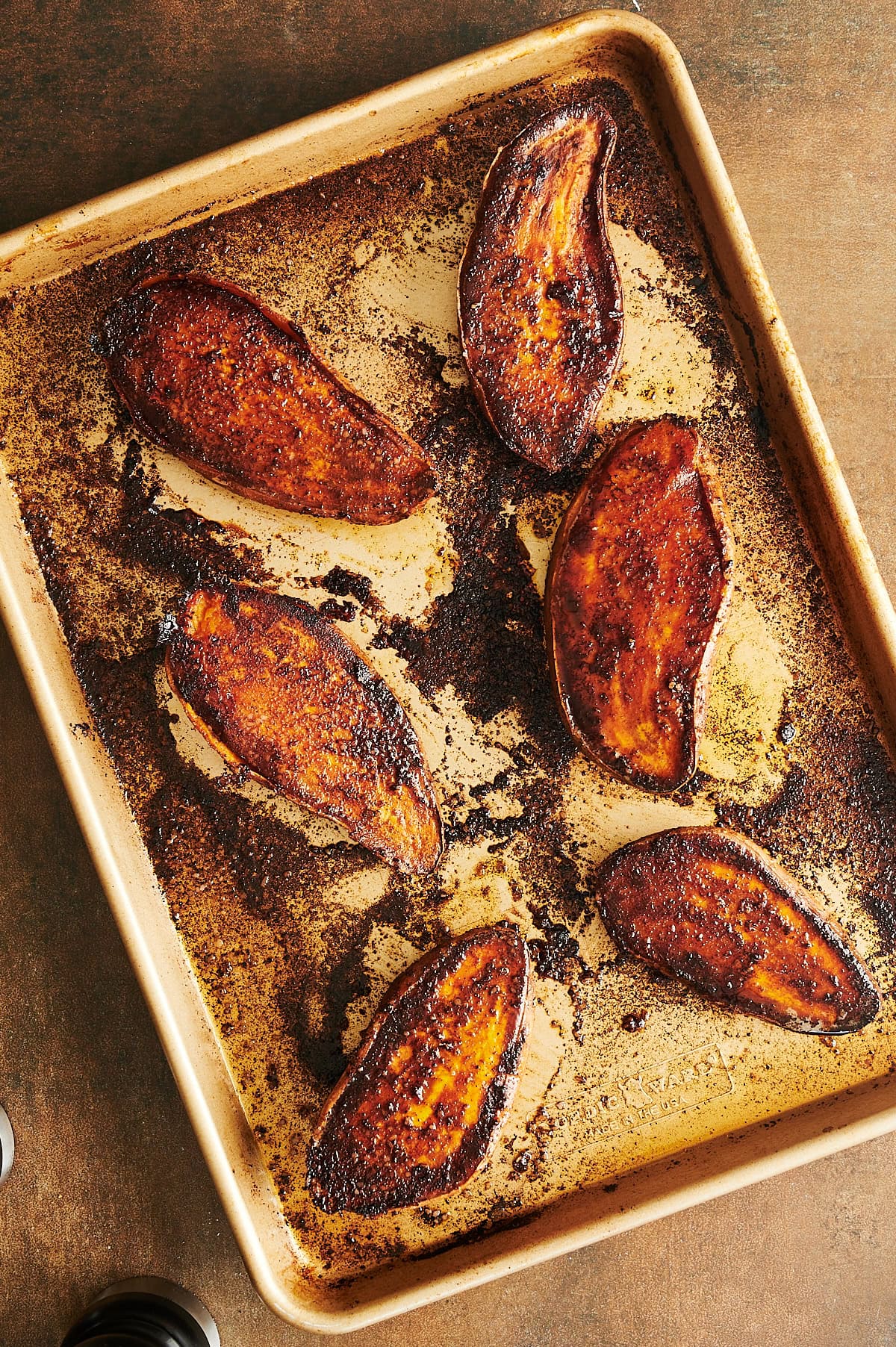 Gold sheet pan with roasted seasoned and spicy sweet potato halves on it.