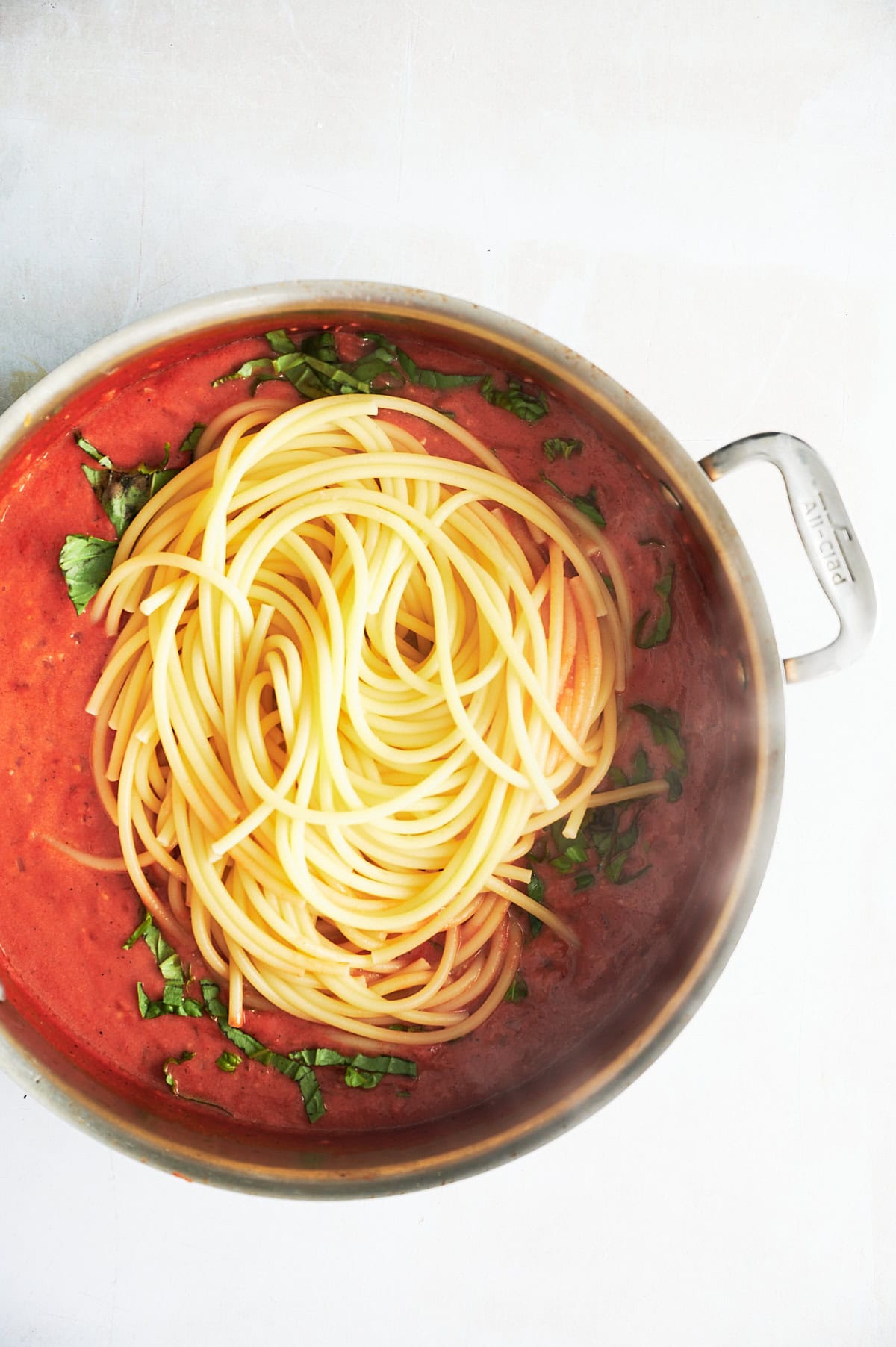 Stainless skillet of tomato basil mascarpone sauce with bucatini being tossed in.