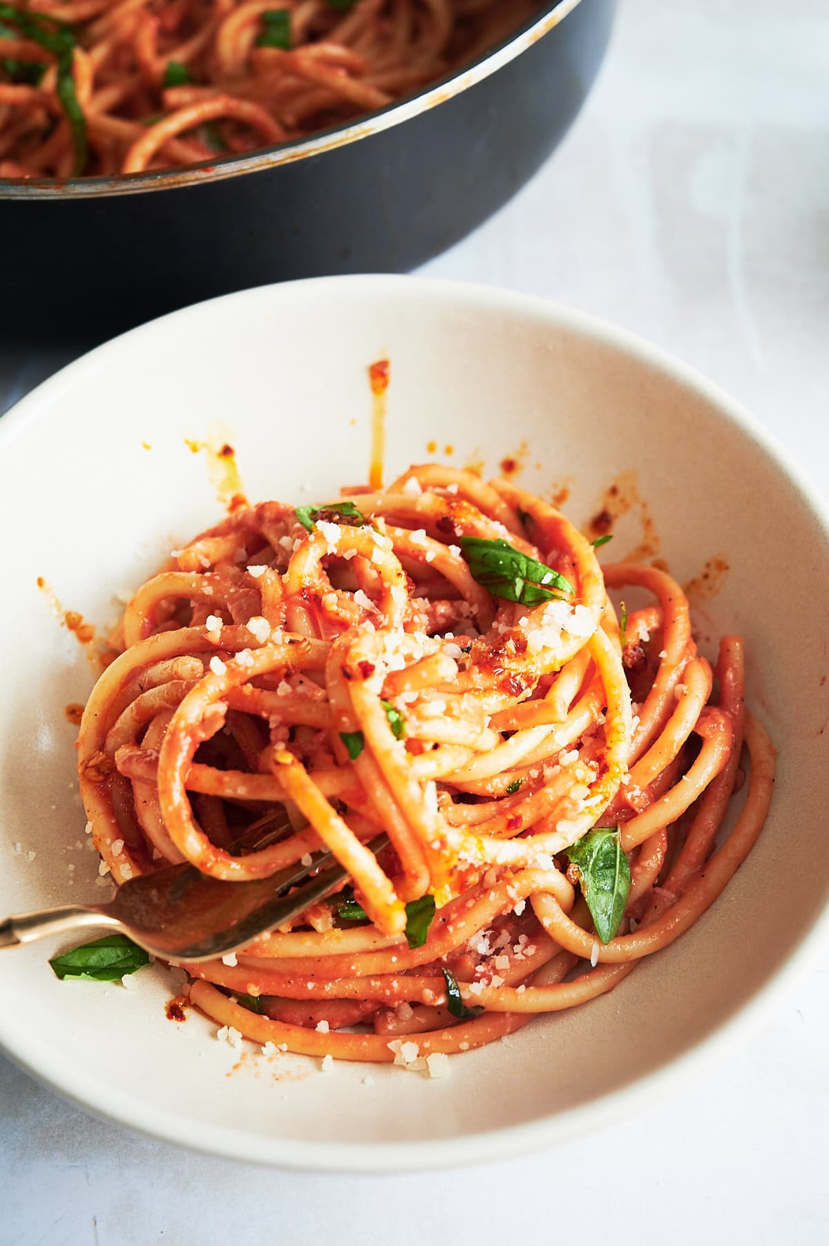 Mascarpone tomato bucatini drizzled with chili oil in a white bowl and sprinkled with basil leaves.