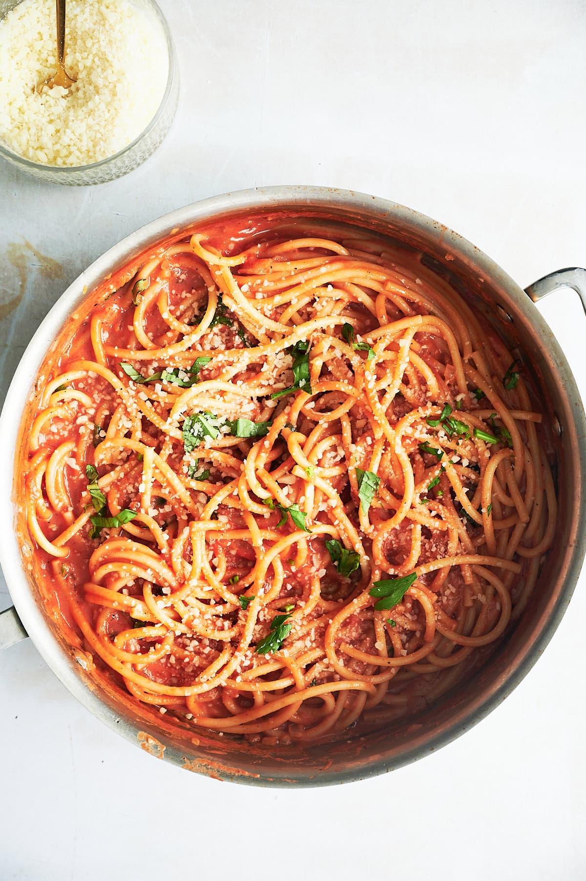 Stainless skillet of bucatini tomato sauce sprinkled with grated parmesan cheese in a bowl.