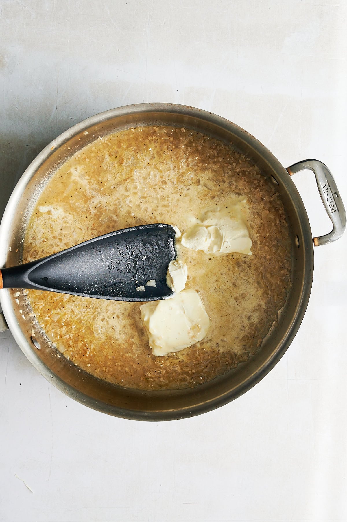 Mascarpone cheese being stirred into onions and garlic for pasta sauce in a stainless skillet.