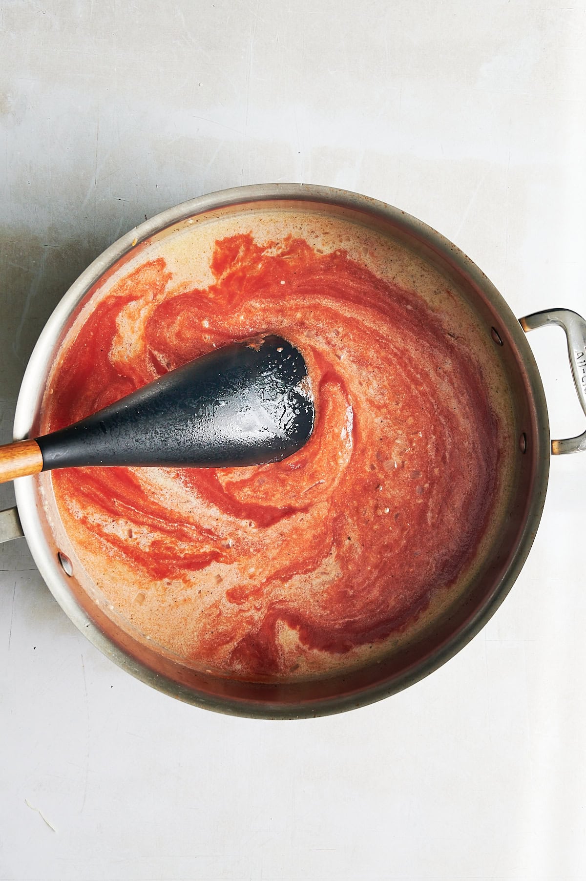 Tomato passata being stirred into mascarpone and onion sauce in a stainless skillet.