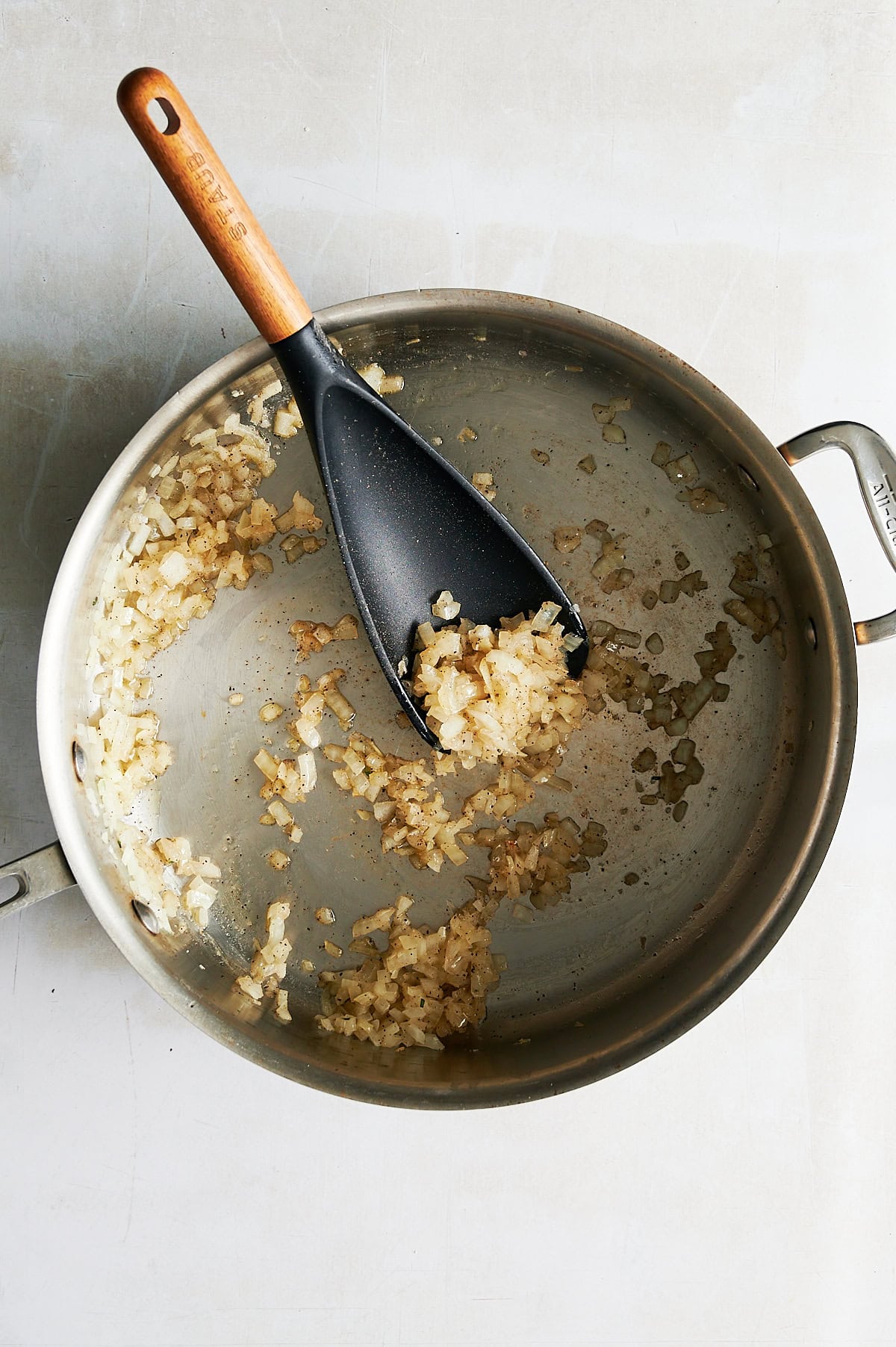 Stainless skillet of sauteed onions with a black and wooden spatula.