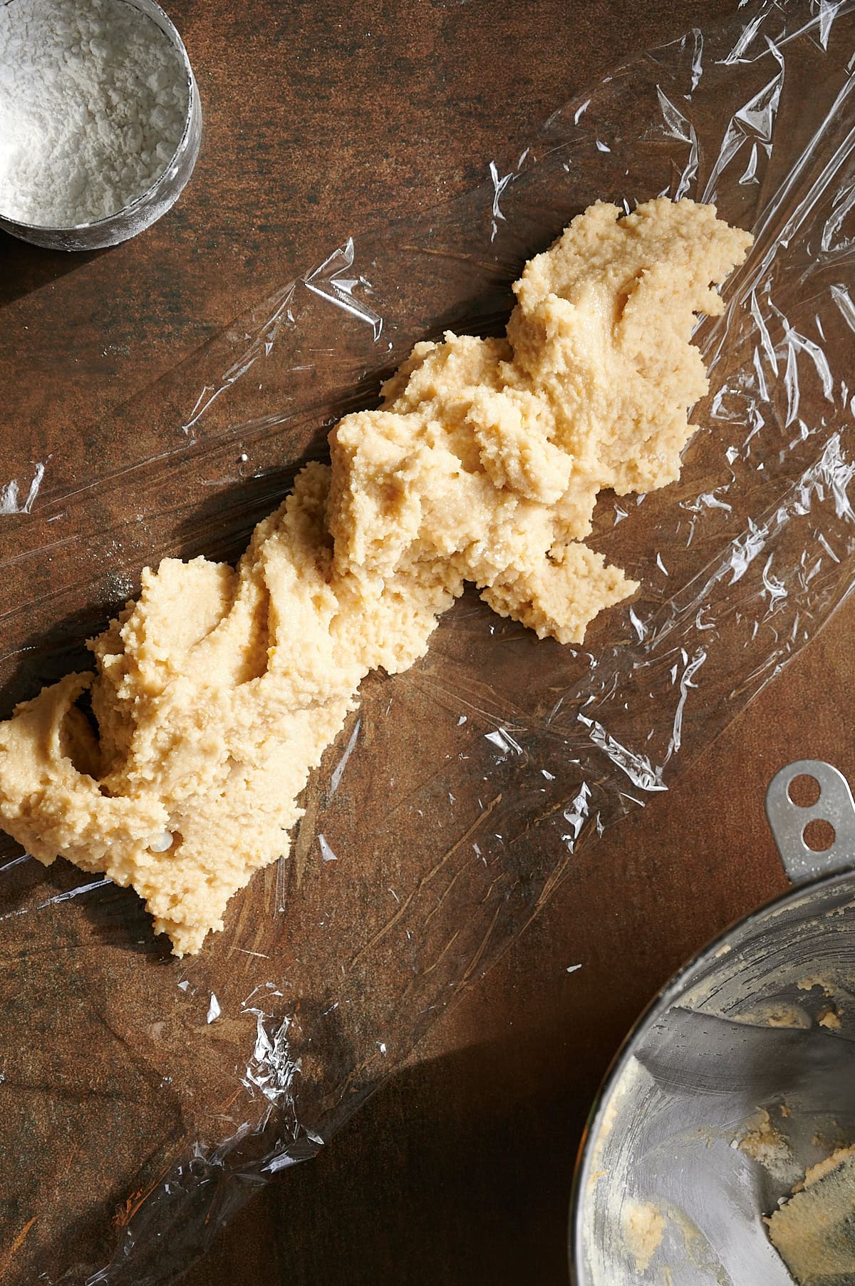 Almond cookie dough being formed into a log on plastic wrap.