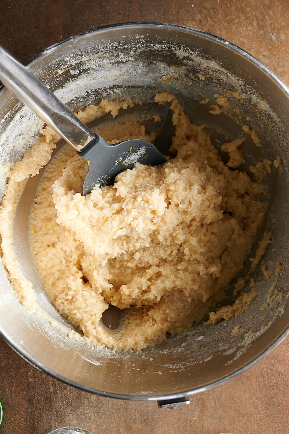 Stand mixer bowl with chewy almond cookie dough being mixed by gray spatula.