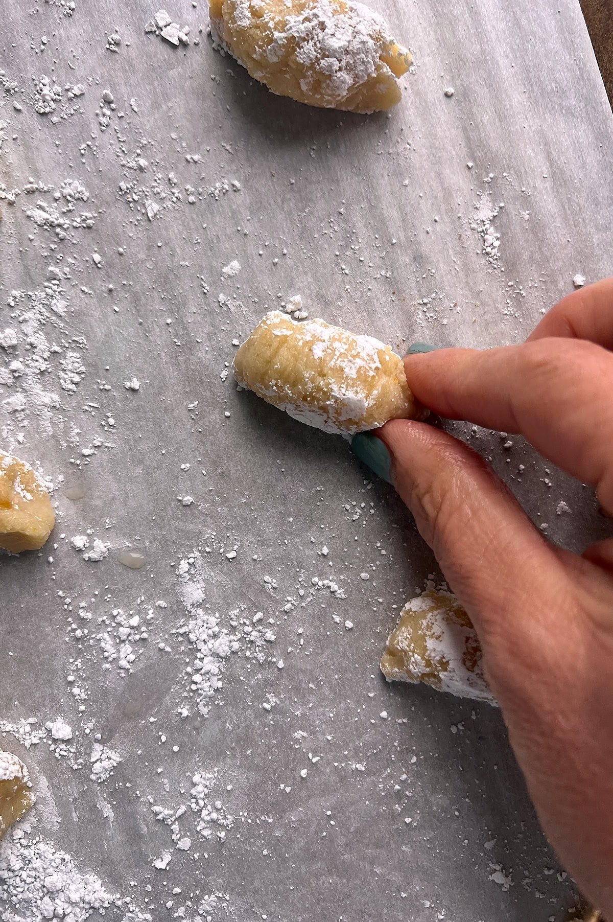 Hand pinching almond cookie dough on powdered sugar parchment paper.