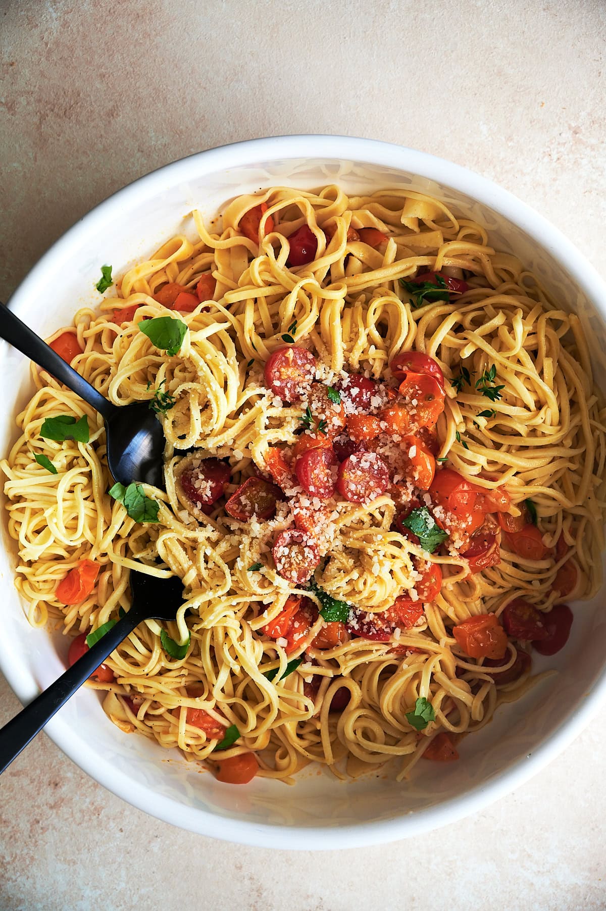 White bowl of chitarra pasta tossed with sugo all'aglione sauce sprinkled with parmesan and basil.