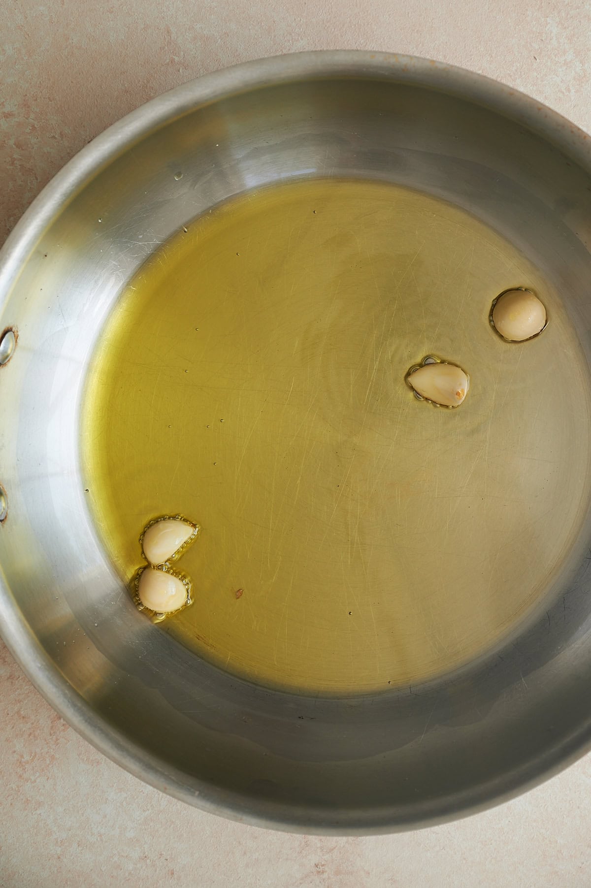 Stainless skillet of olive oil and simmering garlic cloves.