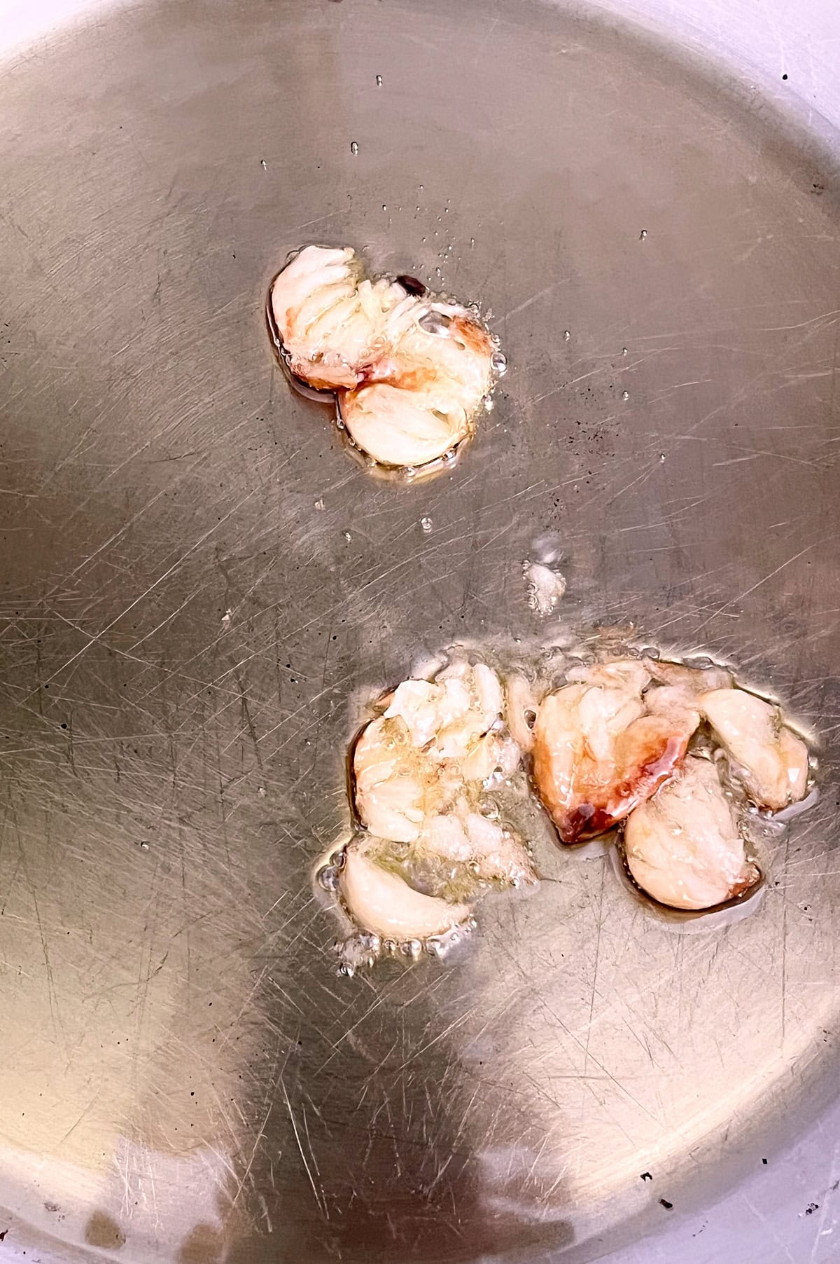 Stainless skillet of olive oil sizzling smashed cloves of garlic.