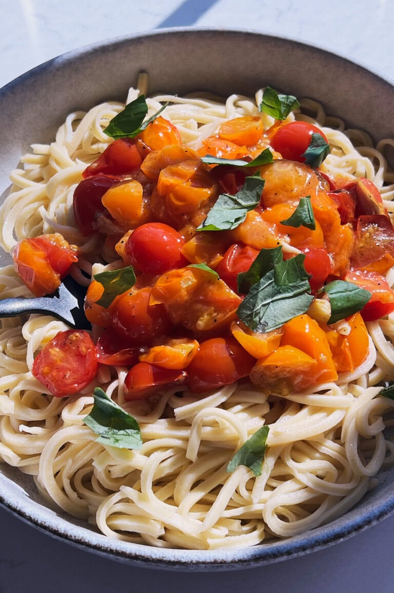 Finished bowl of pasta with garlic tomato sauce and a black fork in it.