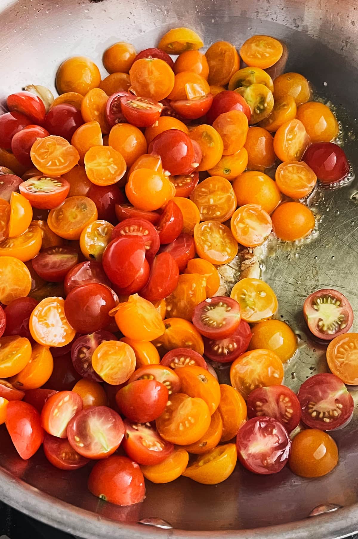 Skillet of olive oil with tomatoes being added to make garlic tomato sauce.