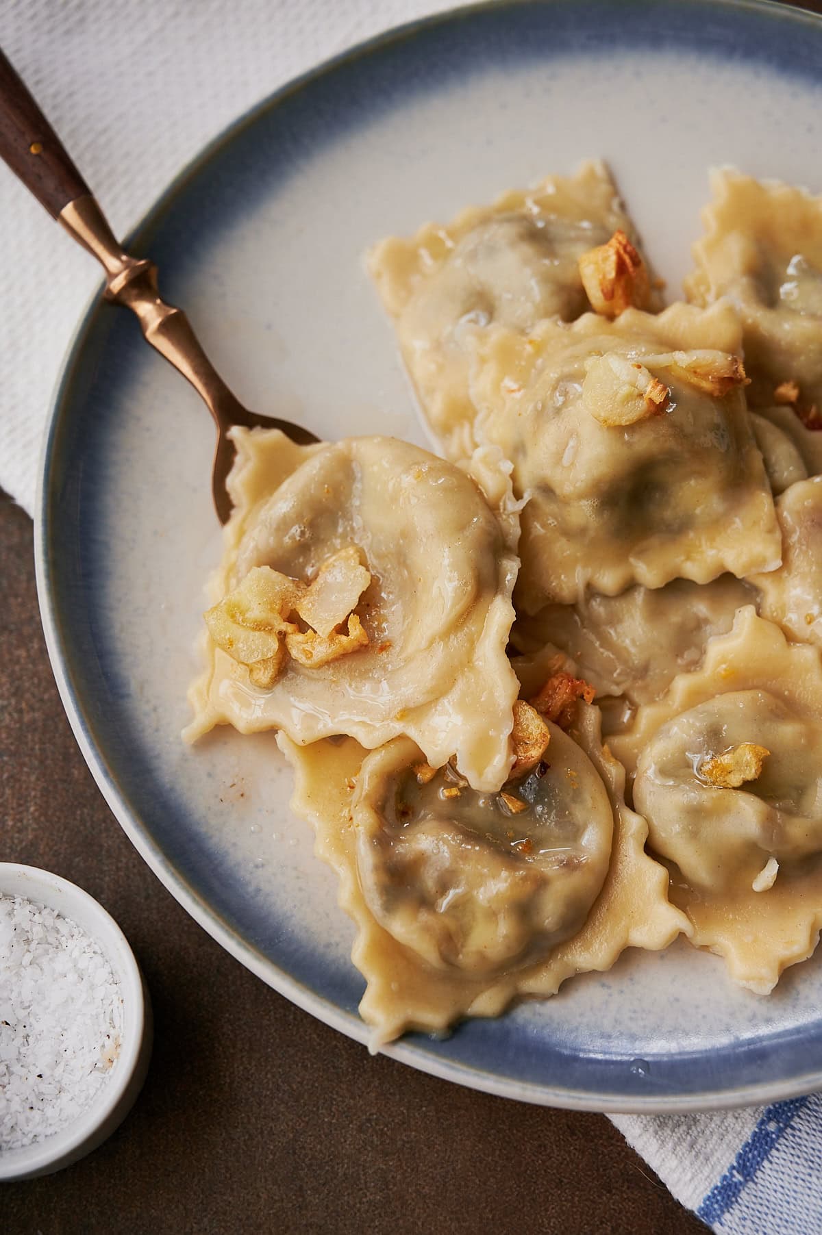 A blue rimmed plate of mushroom ravioli with garlic butter sauce.