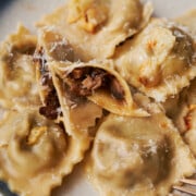 Blue rimmed plate of wild mushroom ravioli with one cut open on the plate.