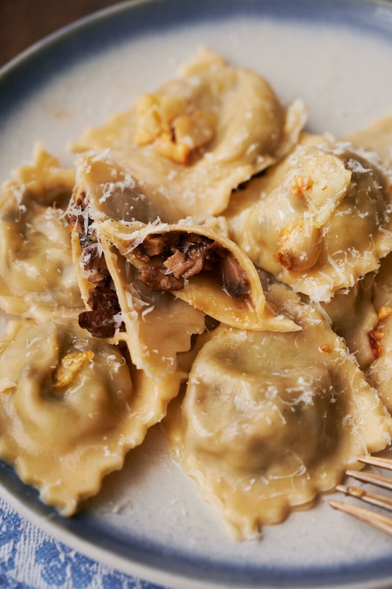 Blue rimmed plate of wild mushroom ravioli with one cut open on the plate.