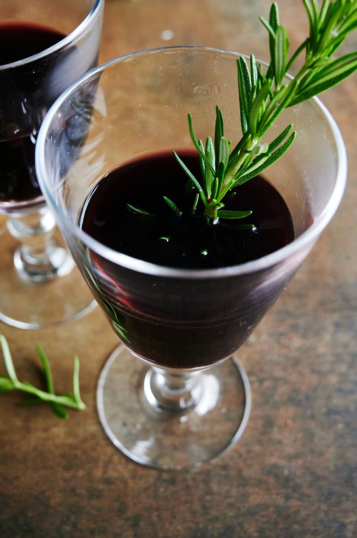 one glass of mulled wine with a sprig of rosemary in it on a brown background.