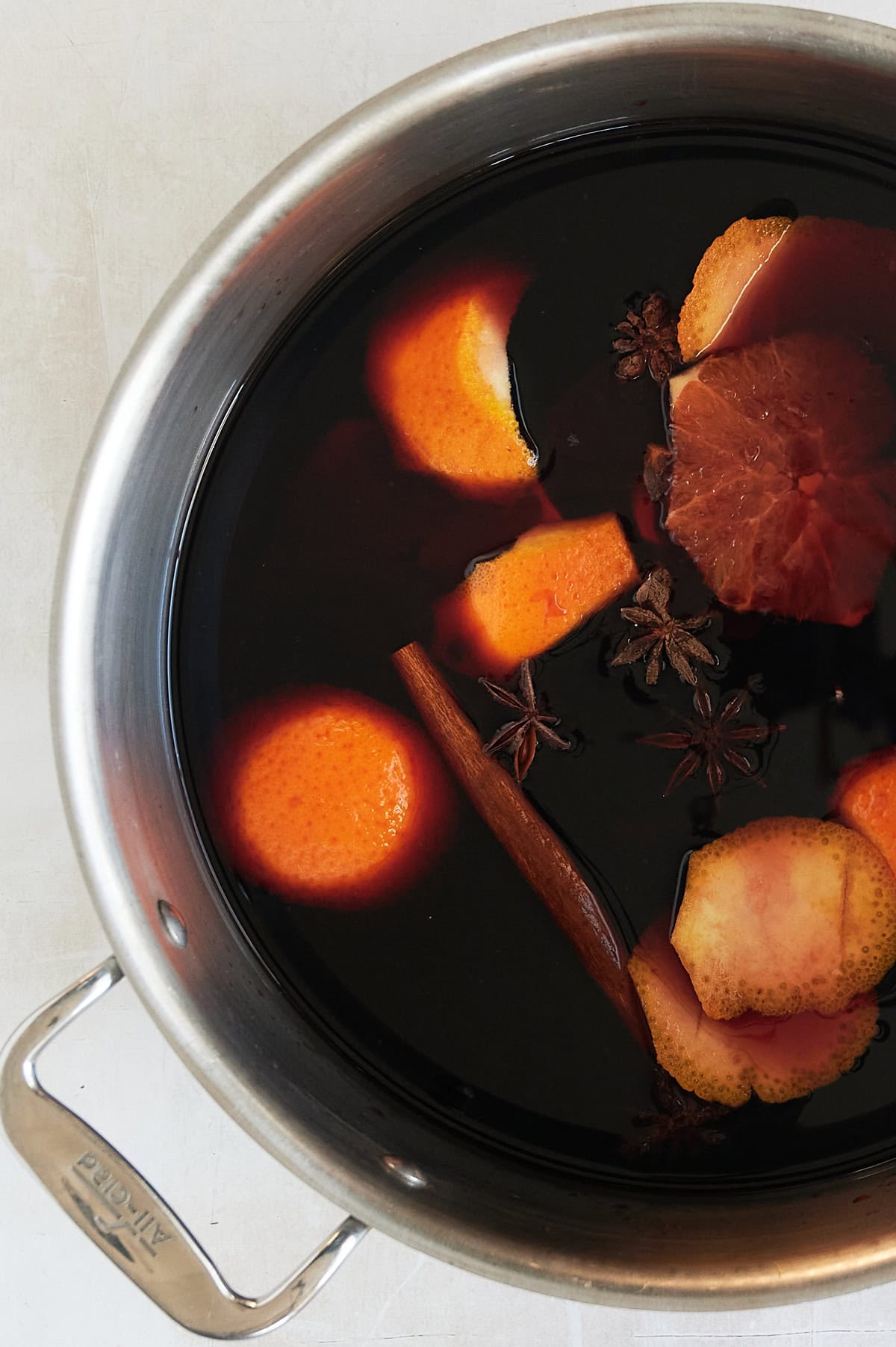 simmering pot of mulled red wine with orange peels, star anise, oranges and cinnamon sticks.