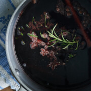 pot of mulled wine with rosemary, star anise, whole cloves and cinnamon sticks on a blue and white dish towel.