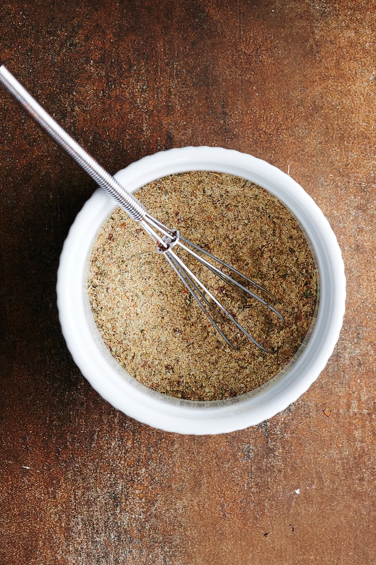 White bowl of seasoning mix being whisked on a brown background.