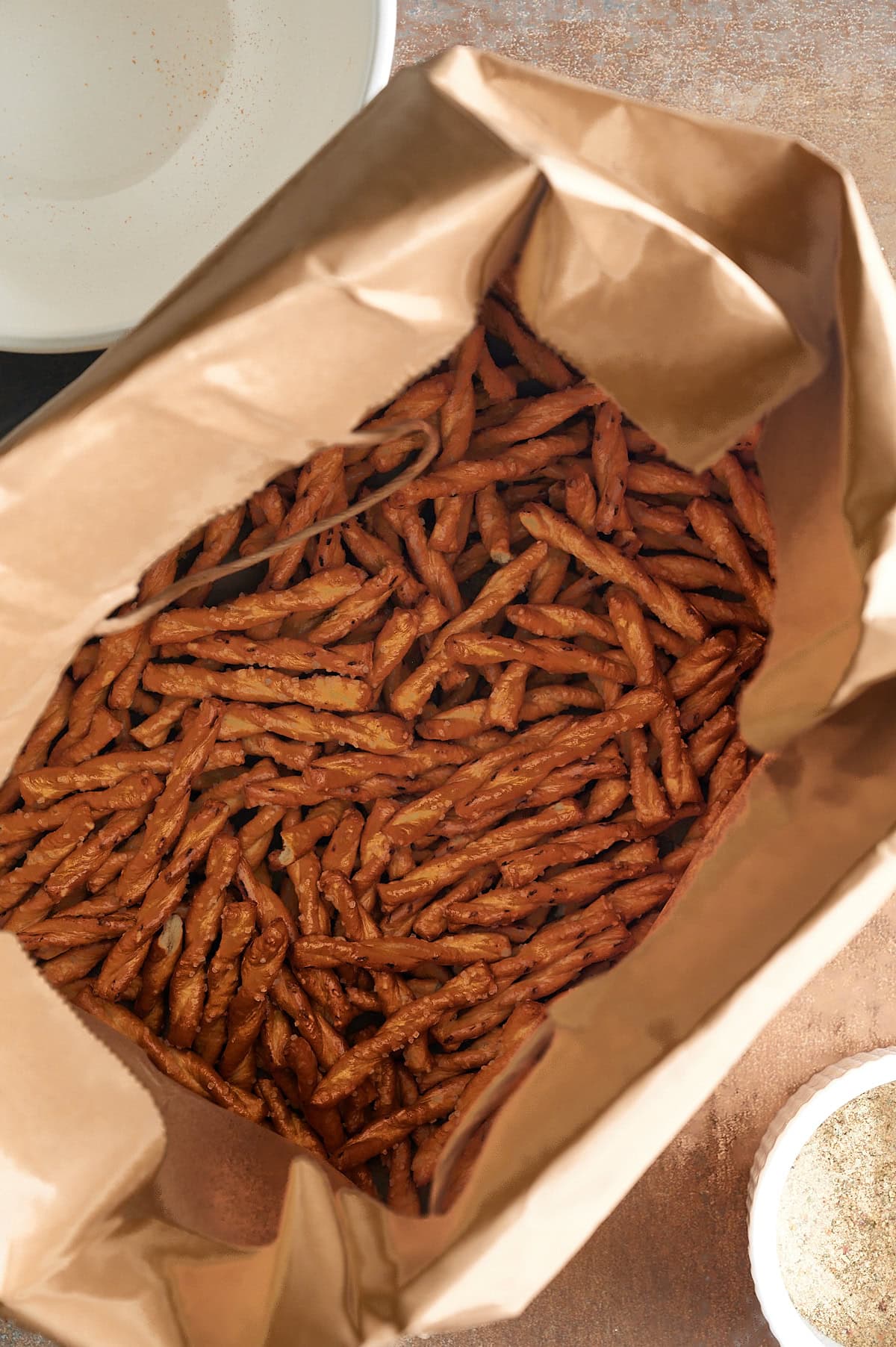 Brown bag with butter braid pretzels inside and bowl of parmesan.