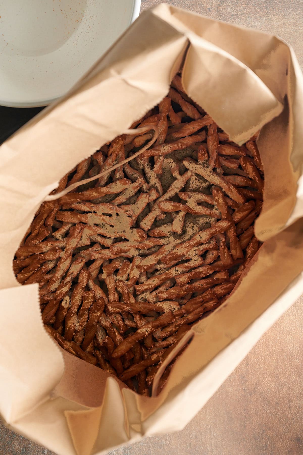 Brown bag with butter braid pretzels inside sprinkled with parmesan garlic seasoning.