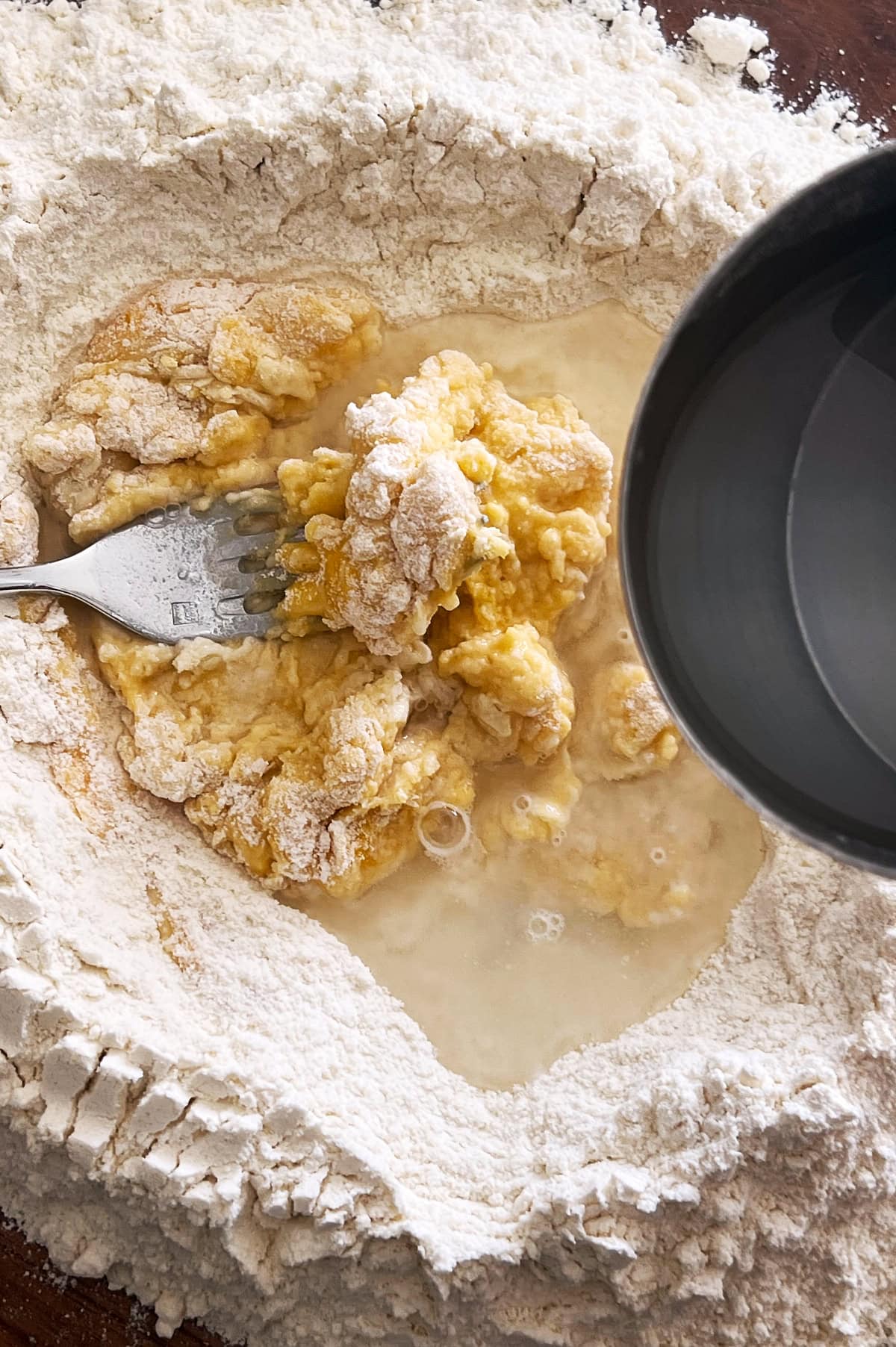 Water being added to eggs and flour to make homemade pasta dough.