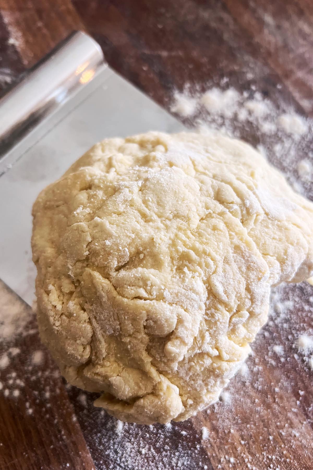 A shaggy just mixed ball of pici dough on a wooden board with a pastry cutter.