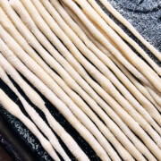 A semolina covered sheet pan of hand rolled pici pasta lined up.