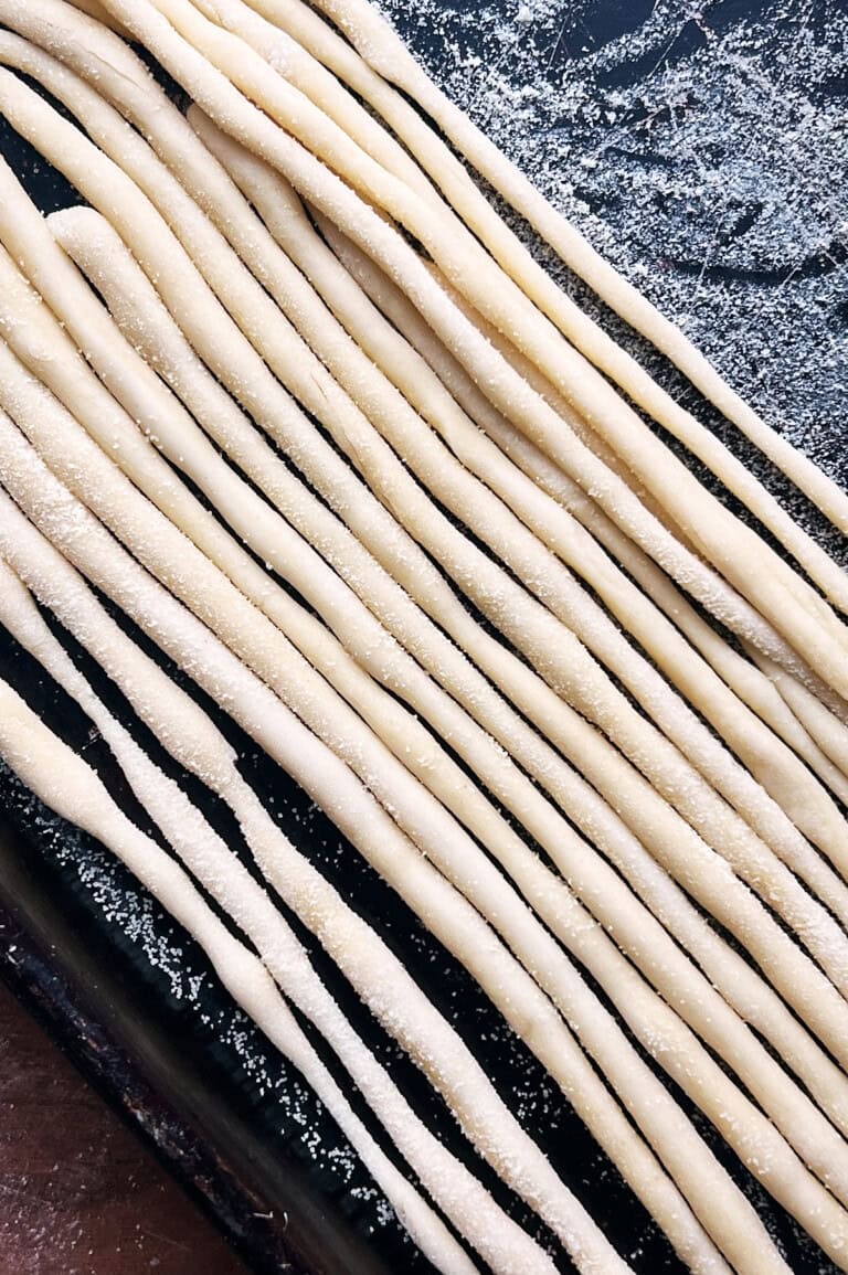 A semolina covered sheet pan of hand rolled pici pasta lined up.
