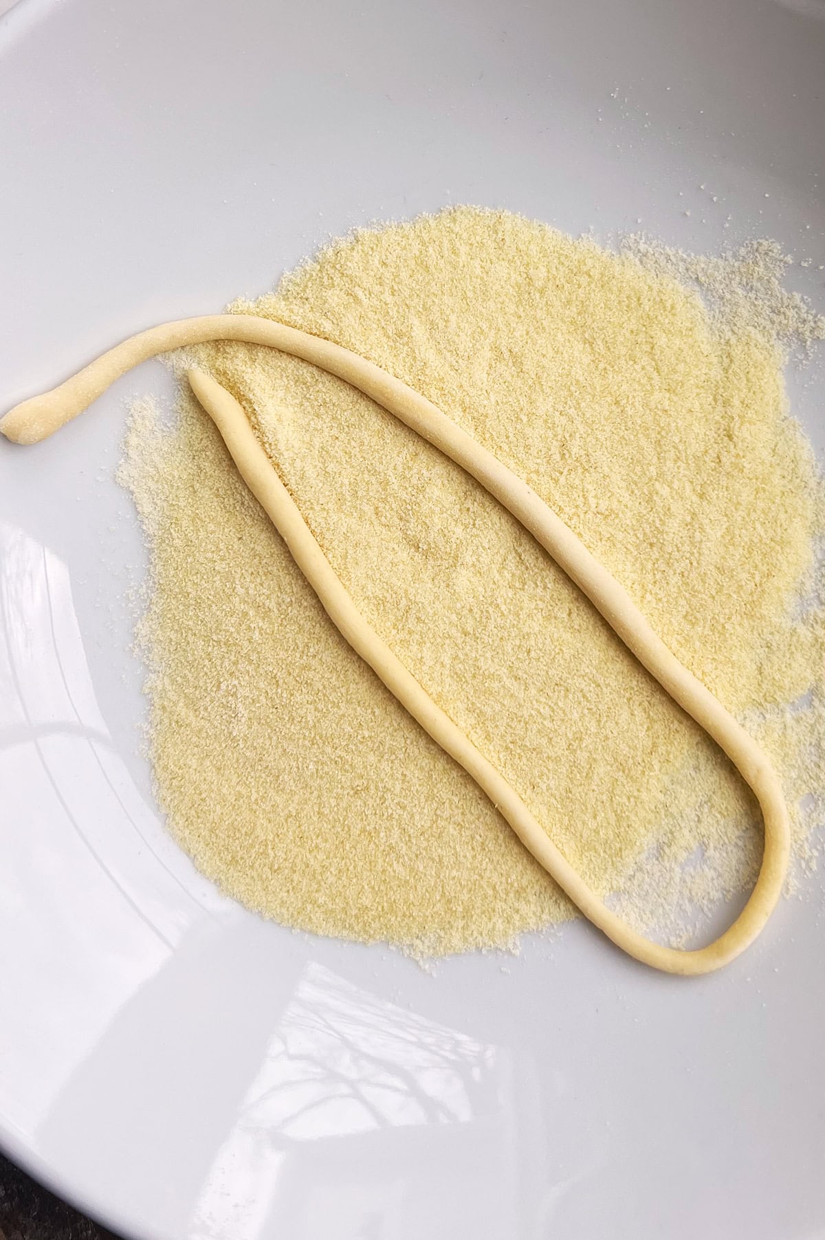 A pici pasta noodle in a white bowl of semolina flour.