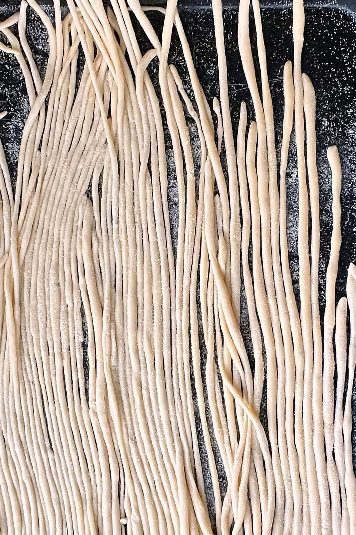Sheet pan of freshly made pici pasta lined up in a row vertically.