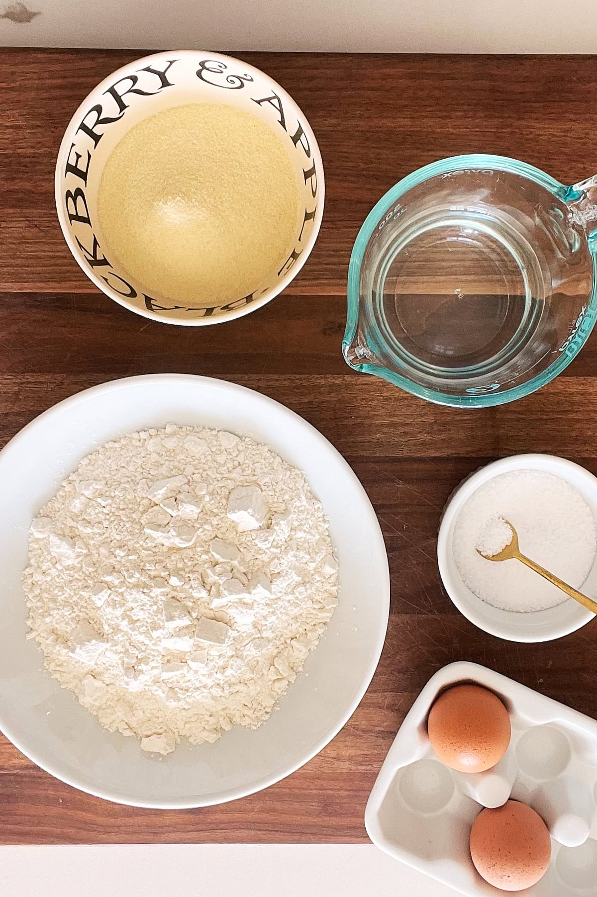 Ingredients to make pici pasta including flour, salt, eggs and water on a wooden board.
